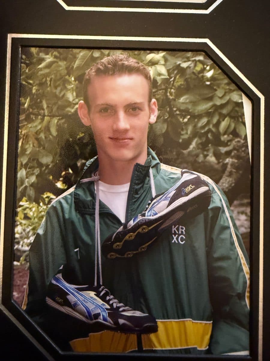 Barrett as a teenager in a green Kent Ridge cross country jacket, holding a pair of track spikes