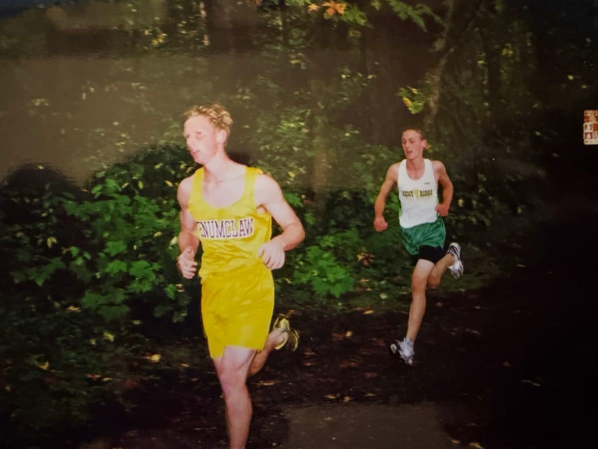 Barrett in a white and green Kent Ridge singlet running a wooded trail behind a runner in yellow