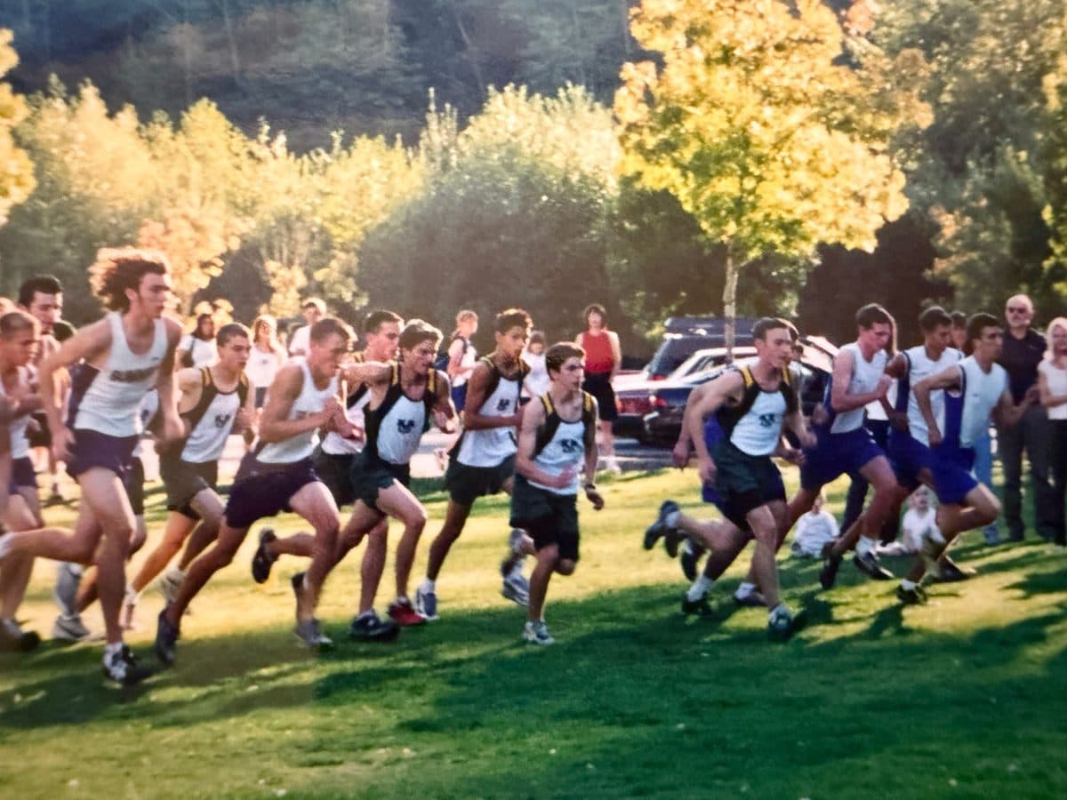 The start of a high school cross country race, a pack of runners sprinting across a grass field